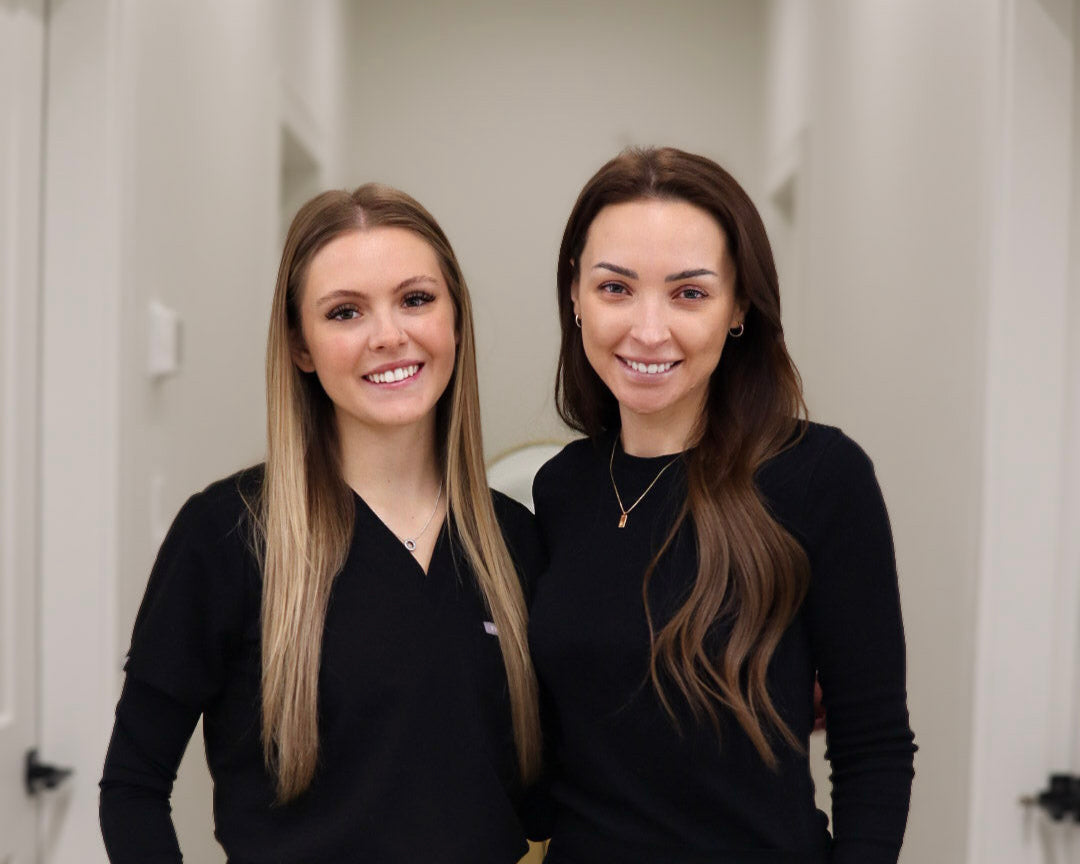 Two women in black scrubs standing in a hallway.